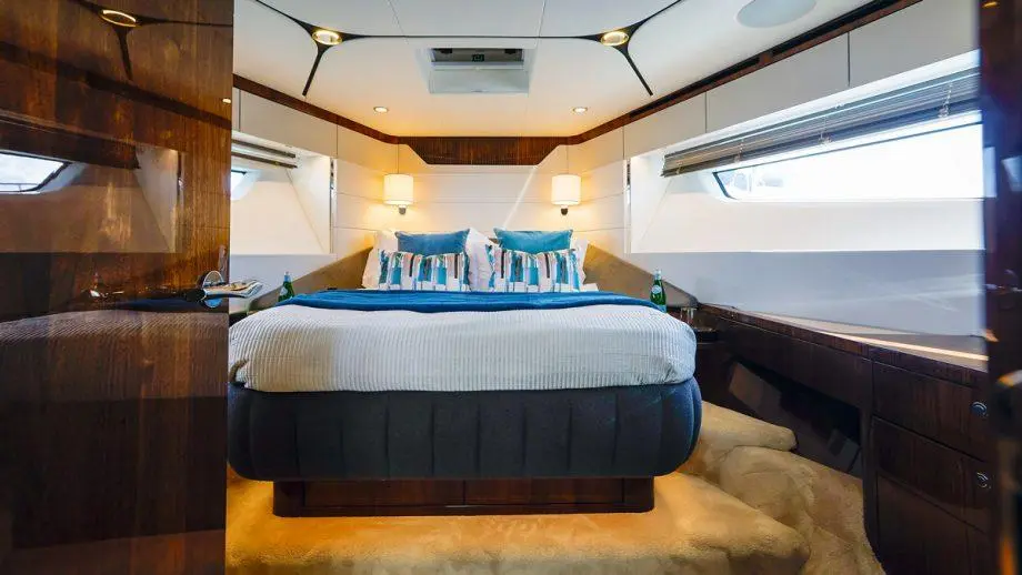 Luxurious boat cabin featuring a large bed with blue and striped cushions, wooden accents, and soft carpeted flooring.